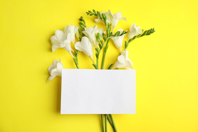 Beautiful spring freesia flowers and blank card on yellow background, flat lay. Space for text