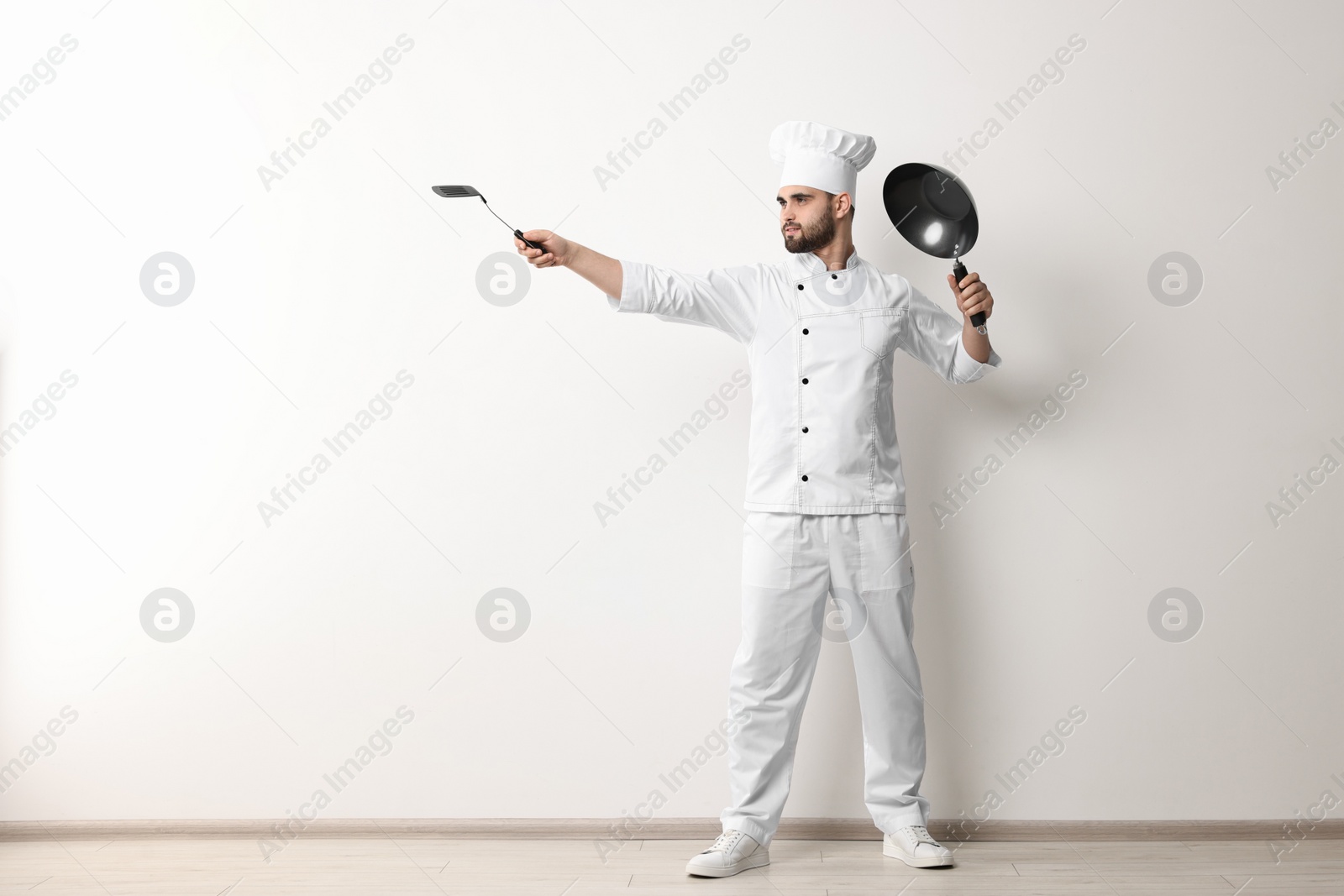 Photo of Professional chef with wok and spatula having fun near white wall indoors. Space for text