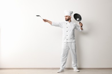 Photo of Professional chef with wok and spatula having fun near white wall indoors. Space for text