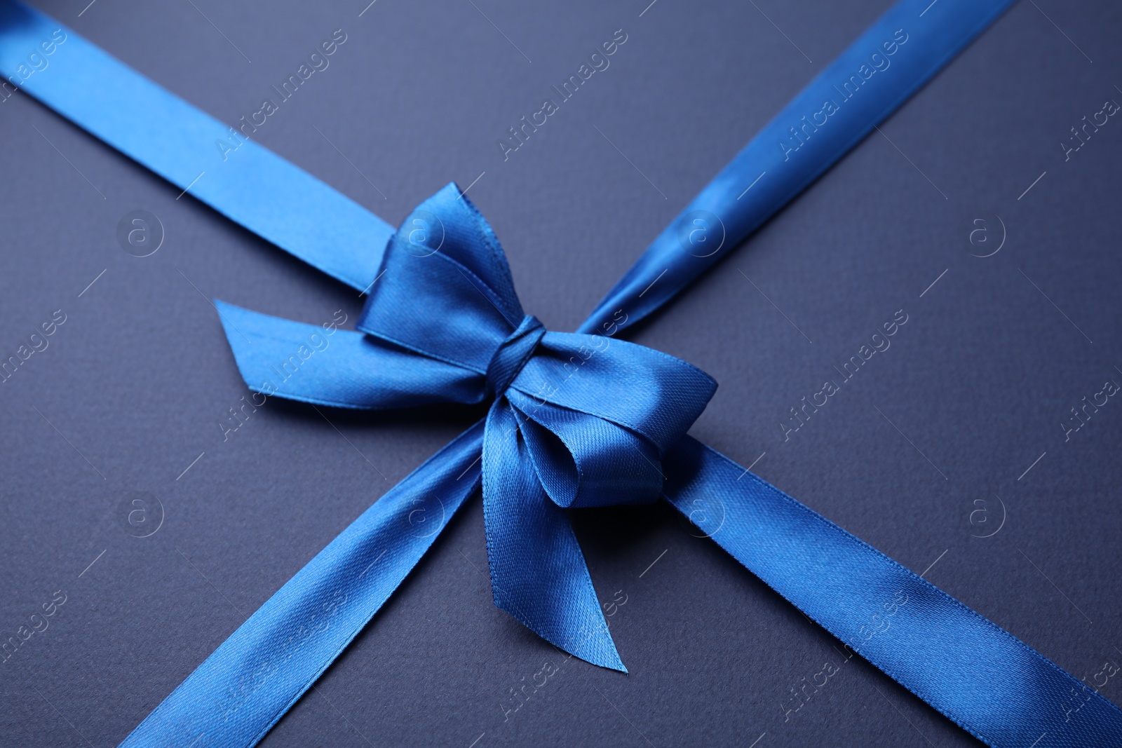 Photo of Bright satin ribbon with bow on blue background