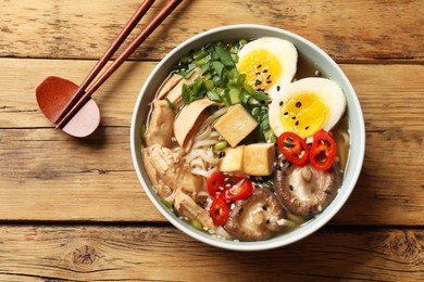 Photo of Noodle soup. Bowl of delicious ramen and chopsticks on wooden table, top view