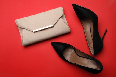 Pair of elegant high heel shoes and handbag on red background, flat lay