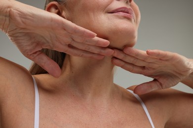 Photo of Mature woman touching her neck on grey background, low angle view