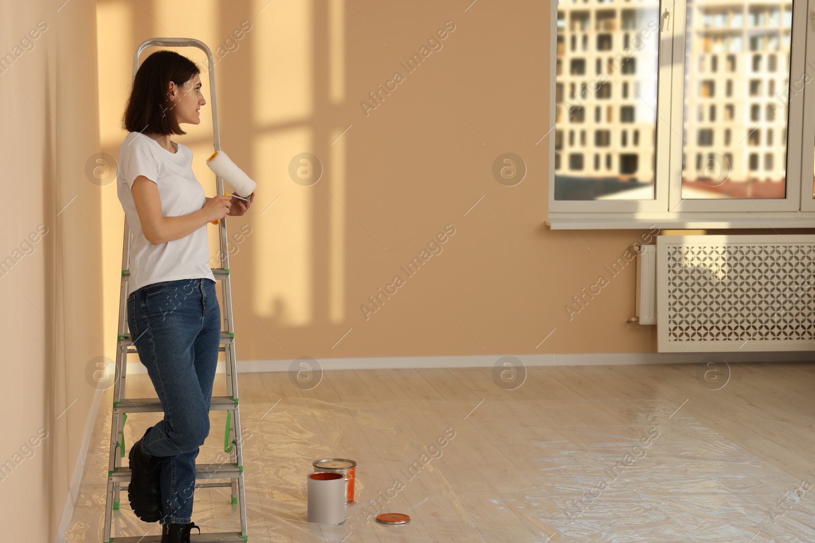 Photo of Young woman with roller near metal stepladder indoors. Room renovation