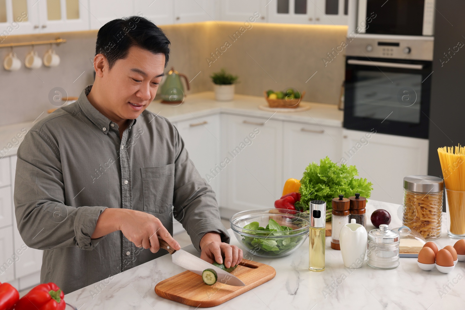Photo of Cooking process. Man cutting fresh cucumber at countertop in kitchen