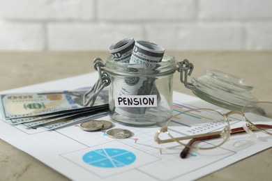 Photo of Glass jar with word Pension, money, chart and glasses on beige table, closeup