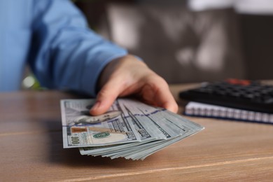 Money exchange. Woman holding dollar banknotes at wooden table, closeup