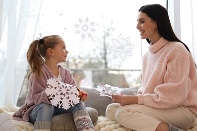 Mother and daughter making paper snowflakes near window at home