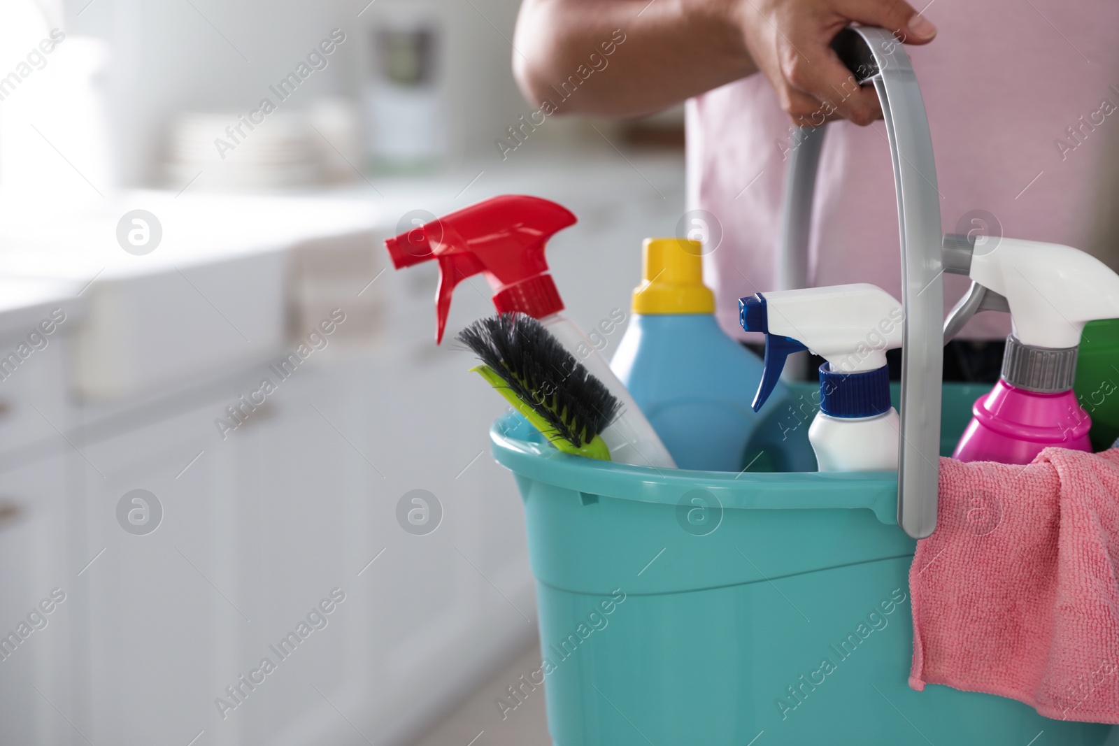 Photo of Woman holding bucket with cleaning supplies in kitchen, closeup. Space for text