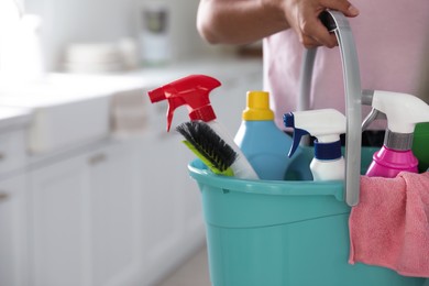 Photo of Woman holding bucket with cleaning supplies in kitchen, closeup. Space for text