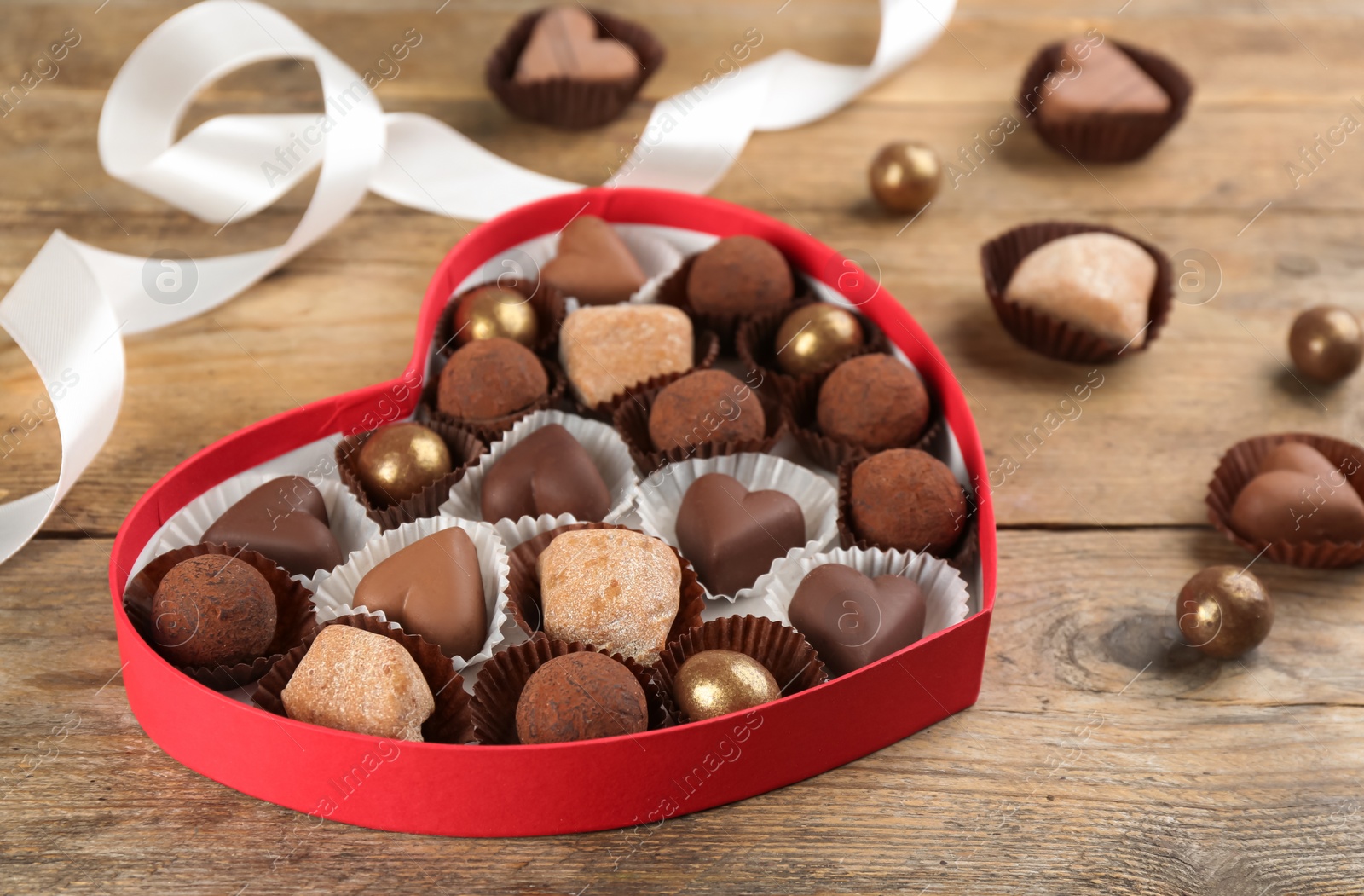 Photo of Different delicious chocolate candies in heart shaped box on wooden table