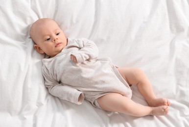 Photo of Cute little baby lying on white sheets, top view