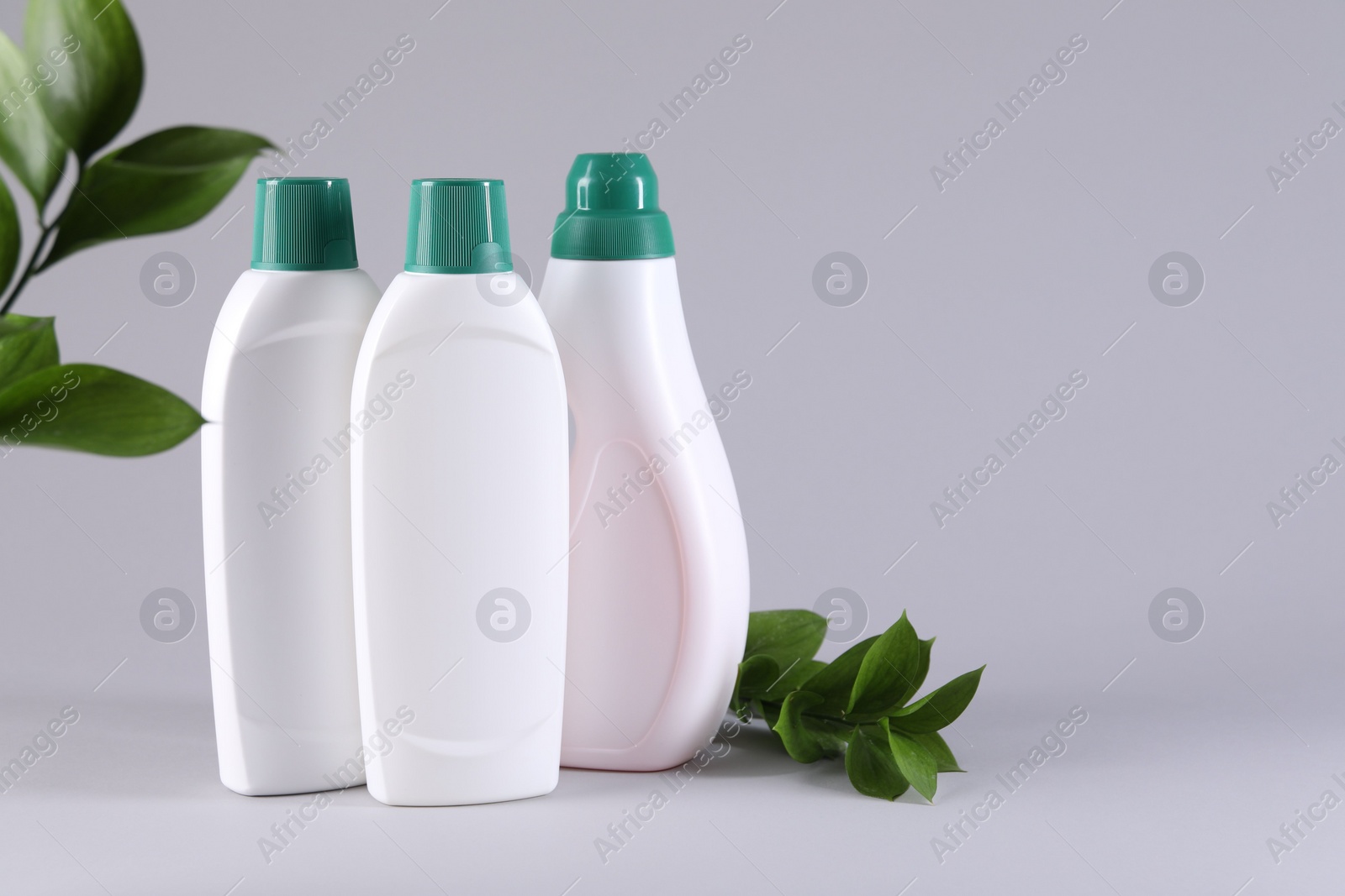 Photo of Bottles of cleaning product and green leaves on light background. Space for text