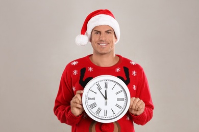 Man in Santa hat with clock on grey background. New Year countdown