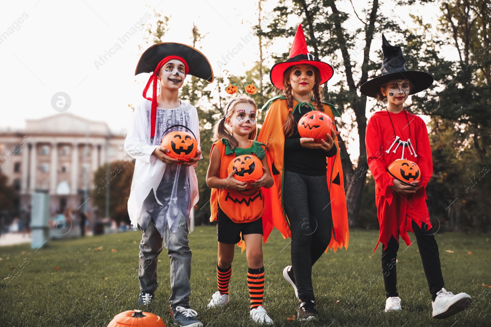 Photo of Cute little kids with pumpkin candy buckets wearing Halloween costumes in park