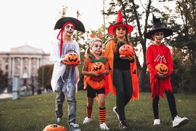 Cute little kids with pumpkin candy buckets wearing Halloween costumes in park