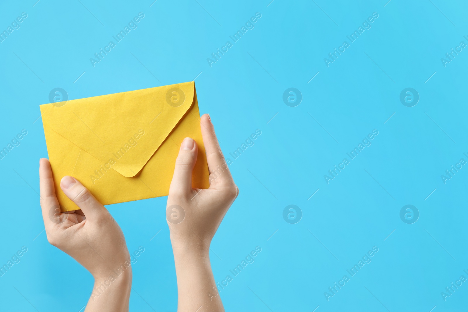 Photo of Woman holding yellow paper envelope on light blue background, closeup. Space for text