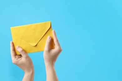 Woman holding yellow paper envelope on light blue background, closeup. Space for text