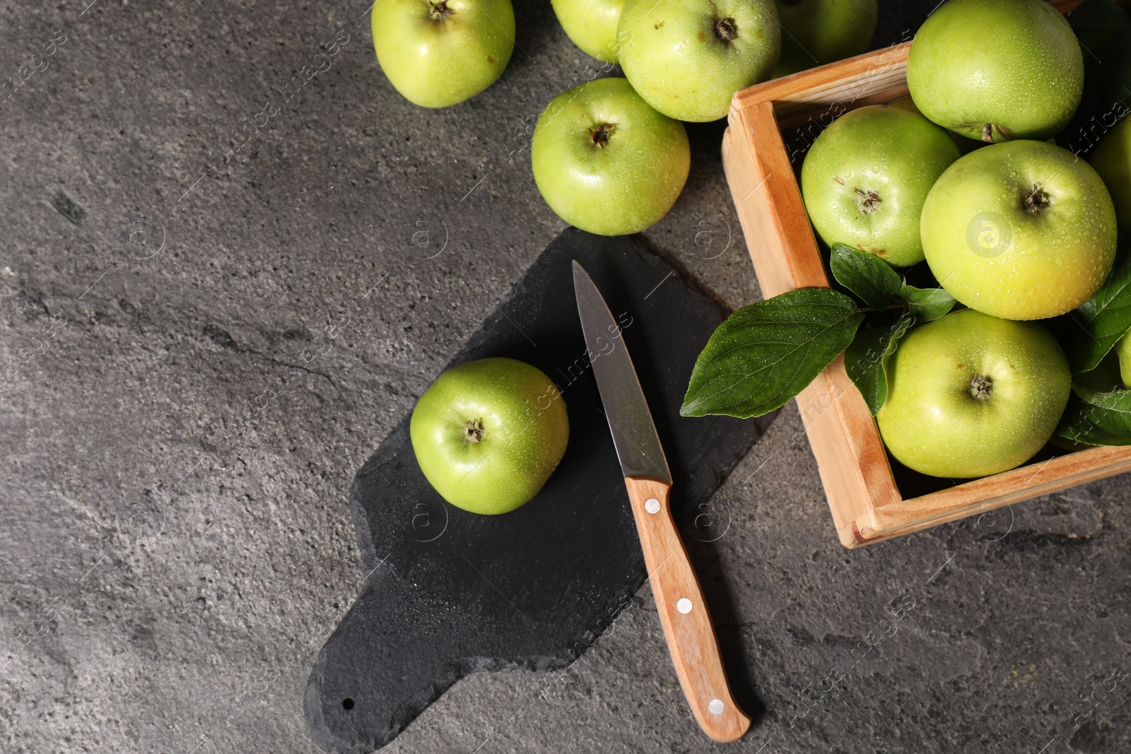 Photo of Ripe green apples with water drops, cutting board and knife on grey table, flat lay. Space for text