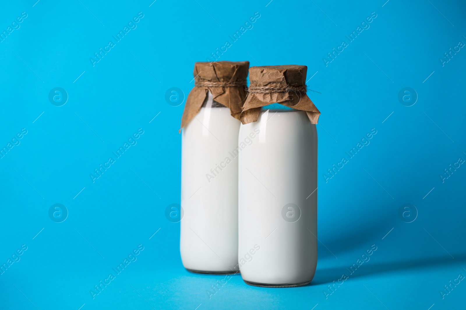 Photo of Tasty fresh milk in bottles on light blue background