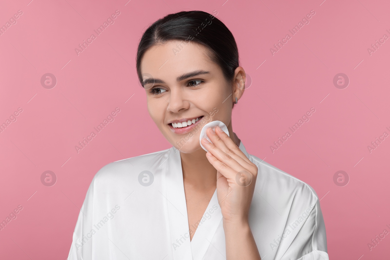 Photo of Young woman cleaning her face with cotton pad on pink background