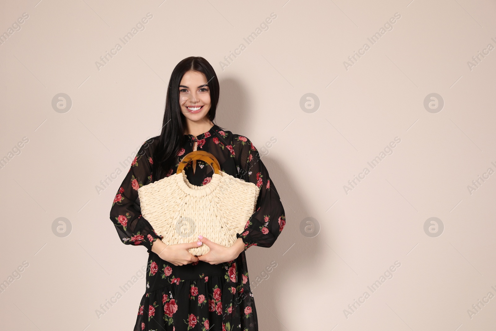 Photo of Young woman wearing floral print dress with straw bag on beige background. Space for text