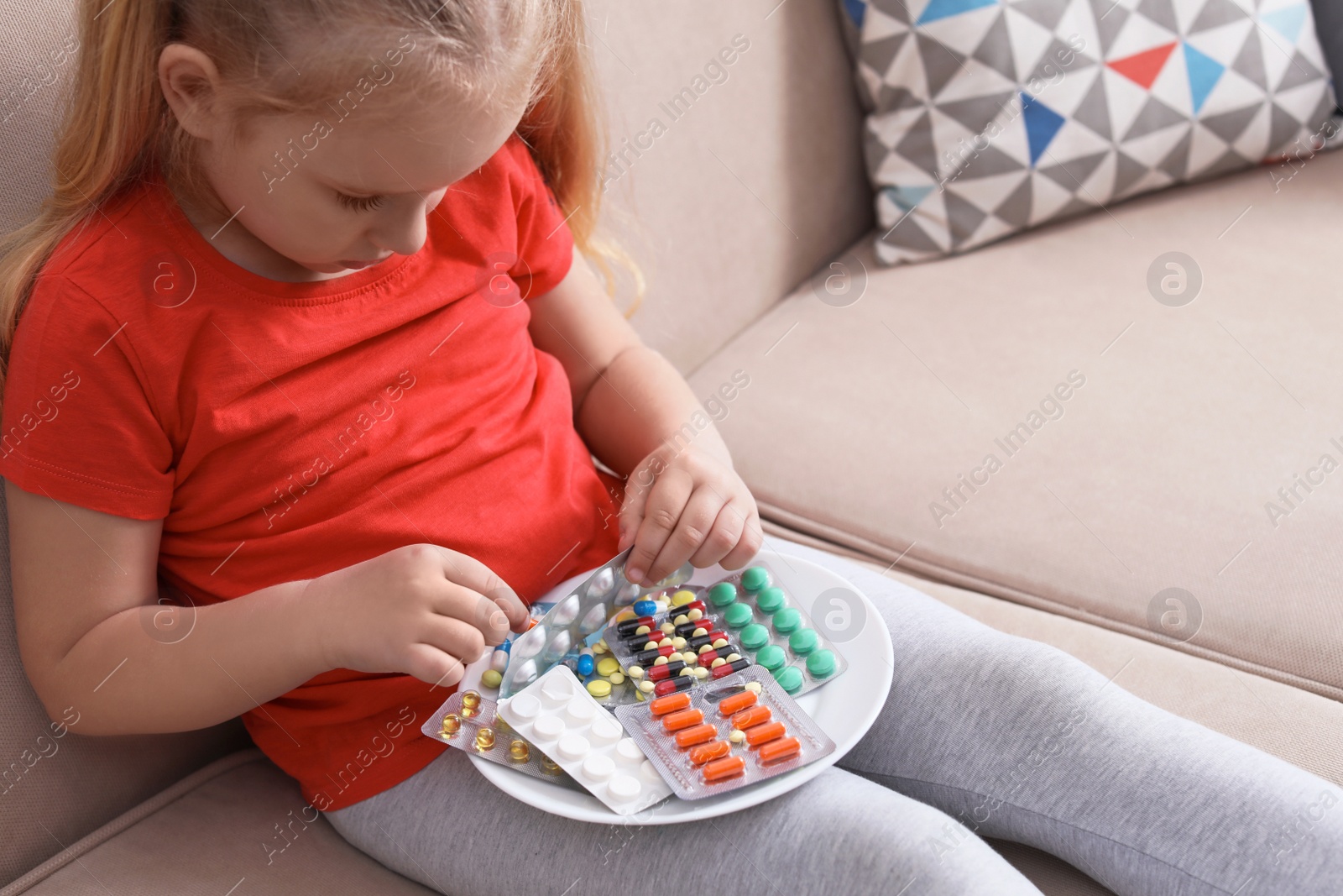 Photo of Little child with plate of different pills at home. Household danger