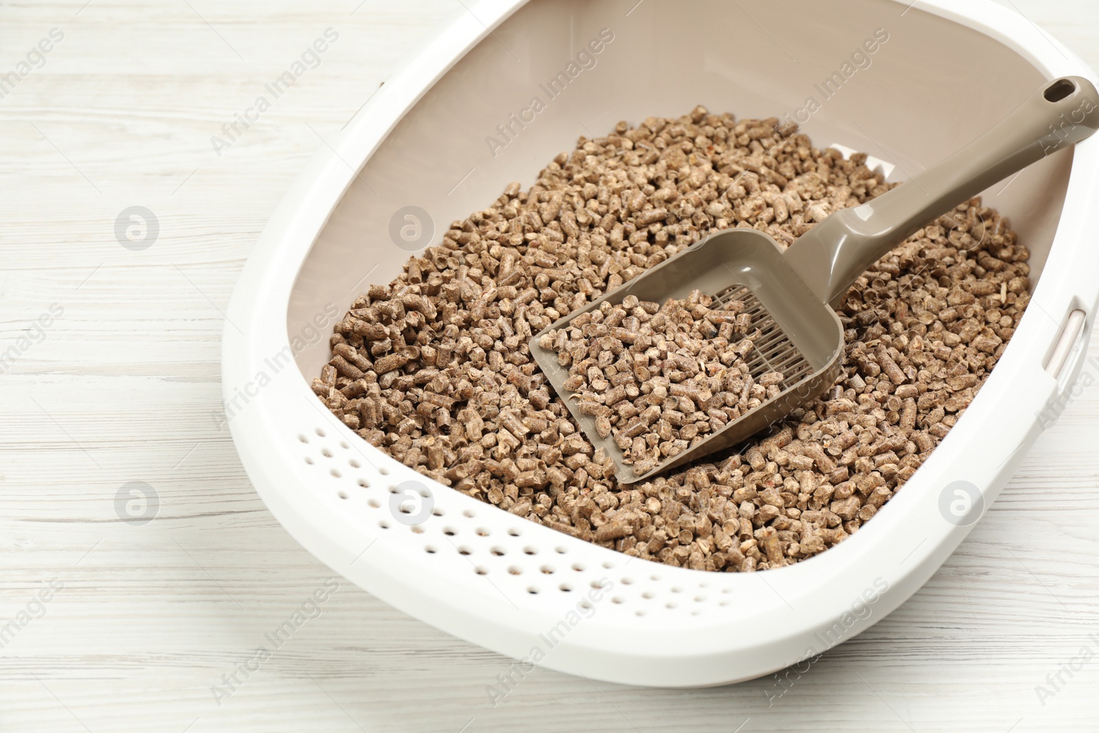 Photo of Cat litter tray with filler and scoop on white wooden floor, closeup