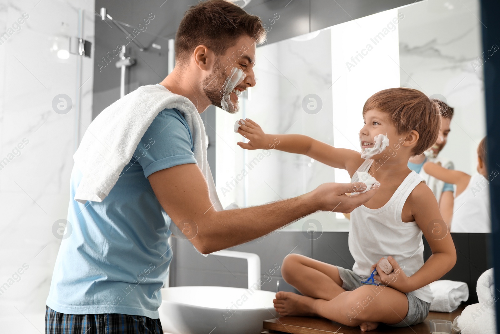 Photo of Dad and son with shaving foam on their faces having fun in bathroom