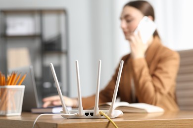 Woman talking on phone while working with laptop at table indoors, focus on Wi-Fi router