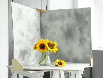 Glass vase with beautiful sunflowers and double-sided backdrops on table in photo studio
