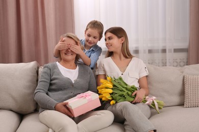 Little girl congratulating her mom and granny with flowers and gift at home. Happy Mother's Day