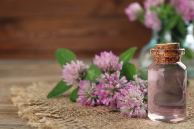 Photo of Beautiful clover flowers and bottle of essential oil on wooden table, closeup. Space for text