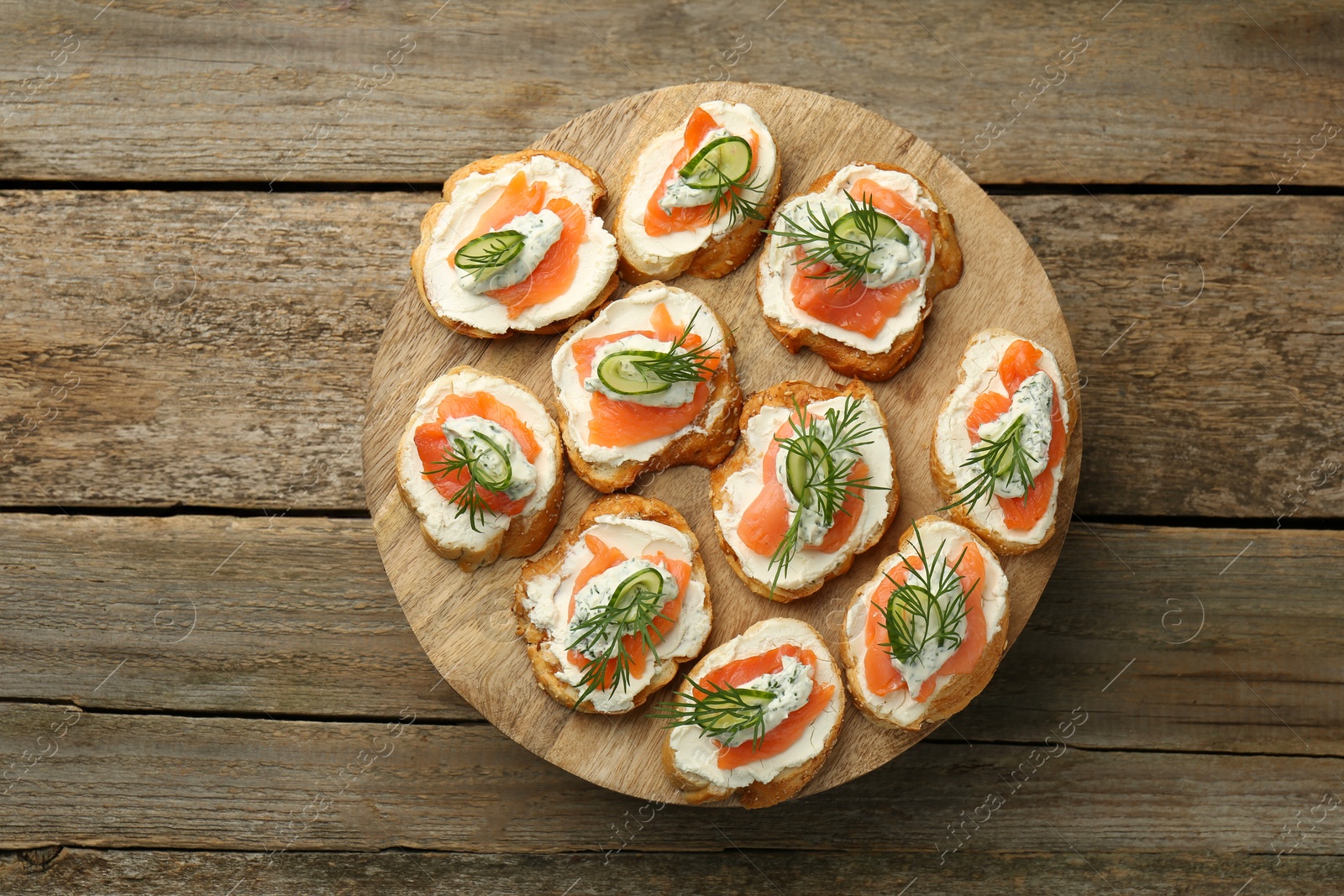 Photo of Tasty canapes with salmon, cucumber, cream cheese and dill on wooden stand, top view