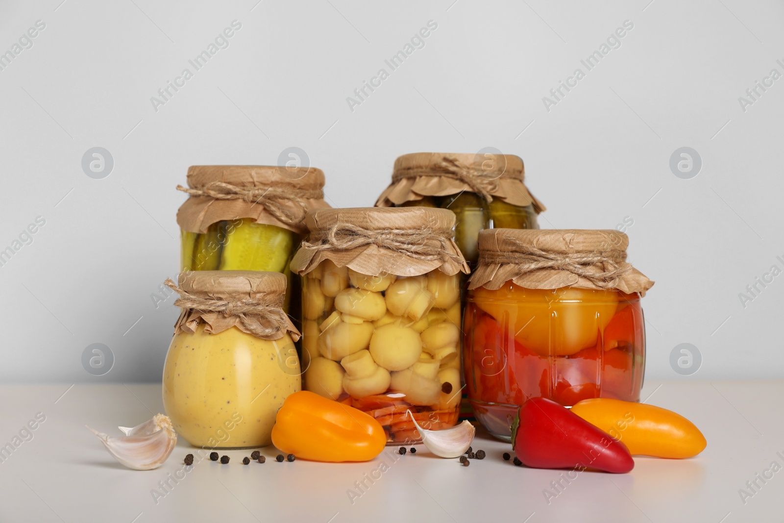 Photo of Jars with different pickled products and fresh peppers on white table