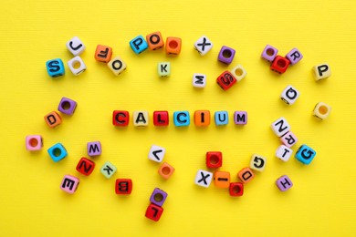 Photo of Word Calcium made of colorful plastic beads with letters on yellow background, top view