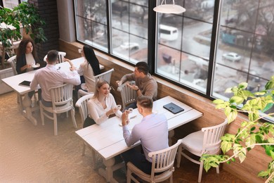 Photo of Coworkers having coffee break near window in cafe, above view