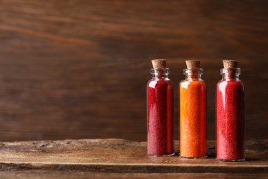 Glass bottles with different food coloring on wooden table. Space for text