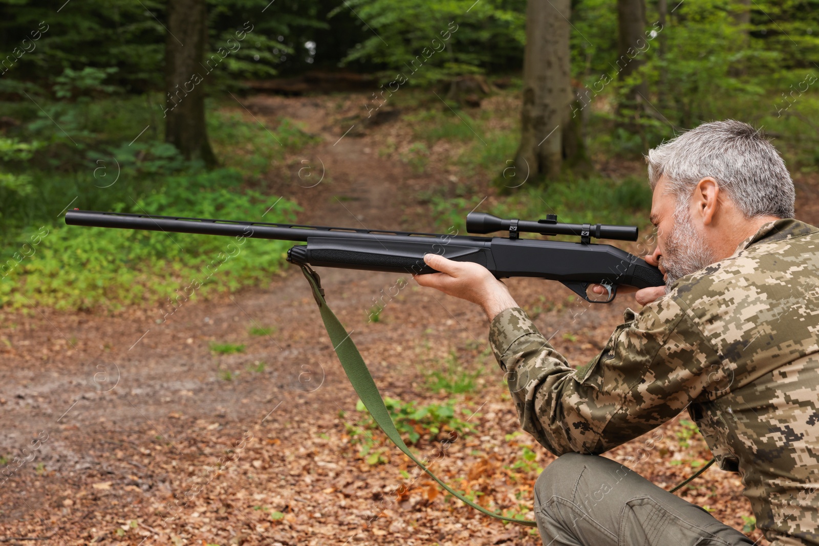 Photo of Man wearing camouflage and aiming with hunting rifle in forest