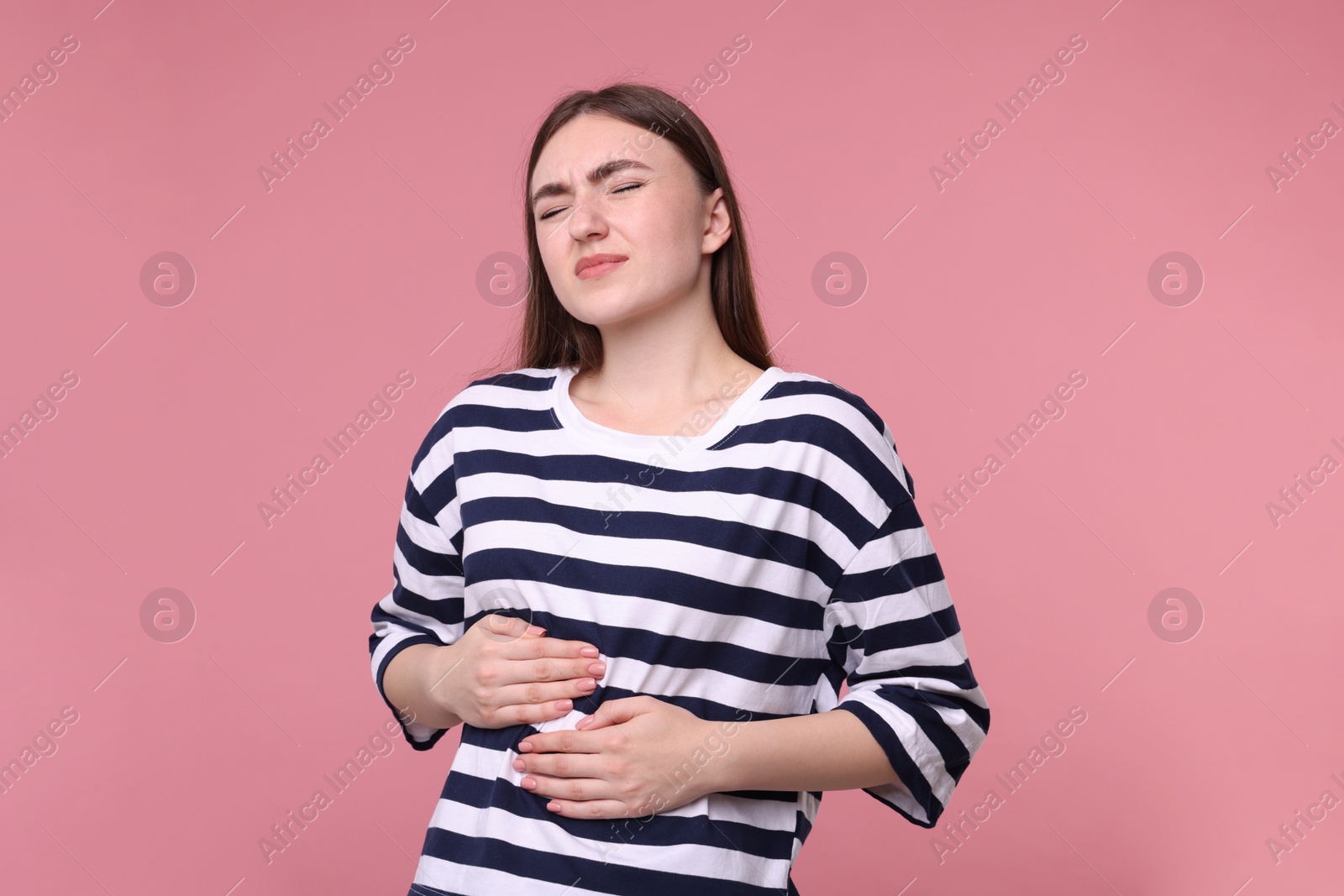 Photo of Young woman suffering from stomach pain on pink background