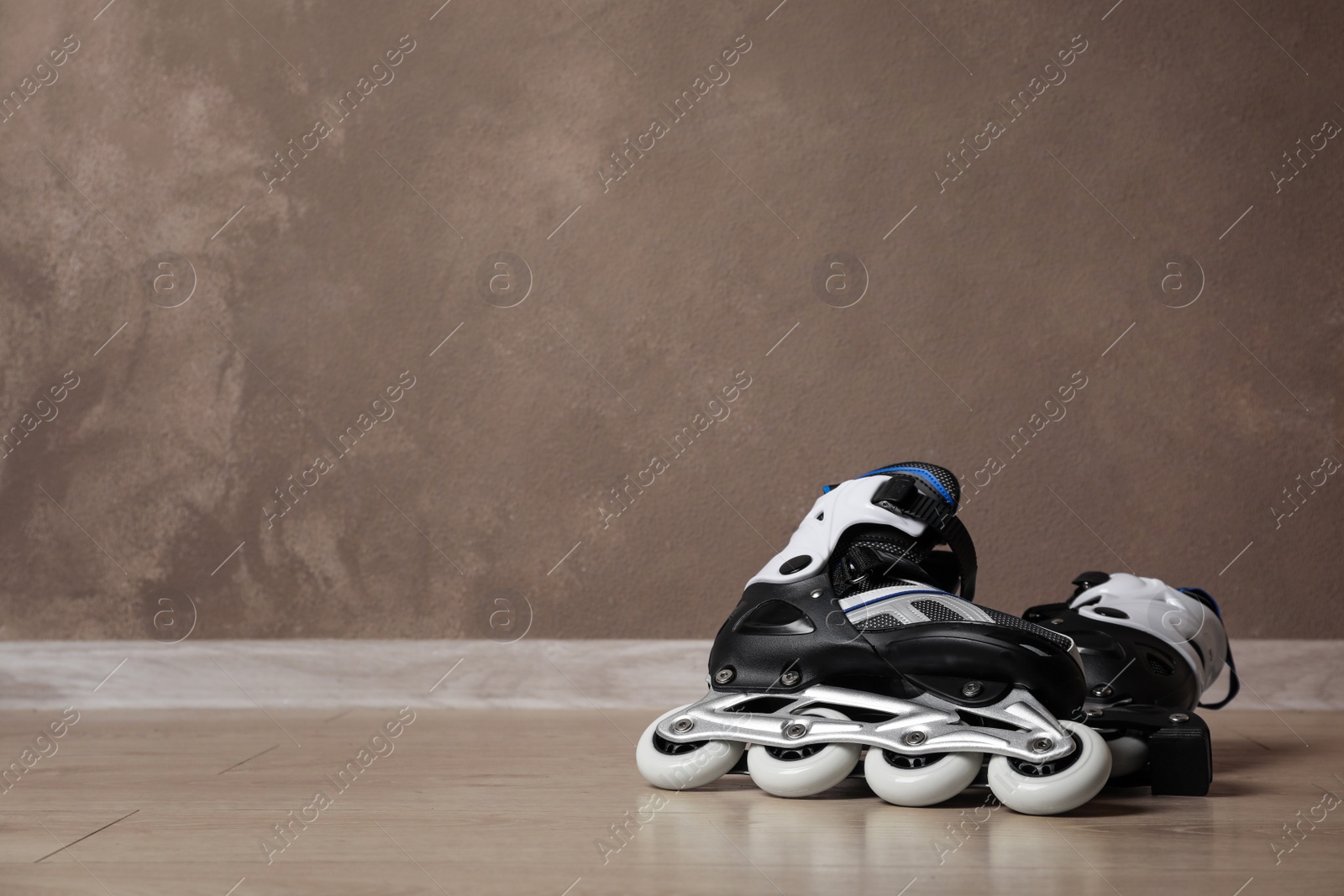 Photo of Inline roller skates on floor near brown wall. Space for text