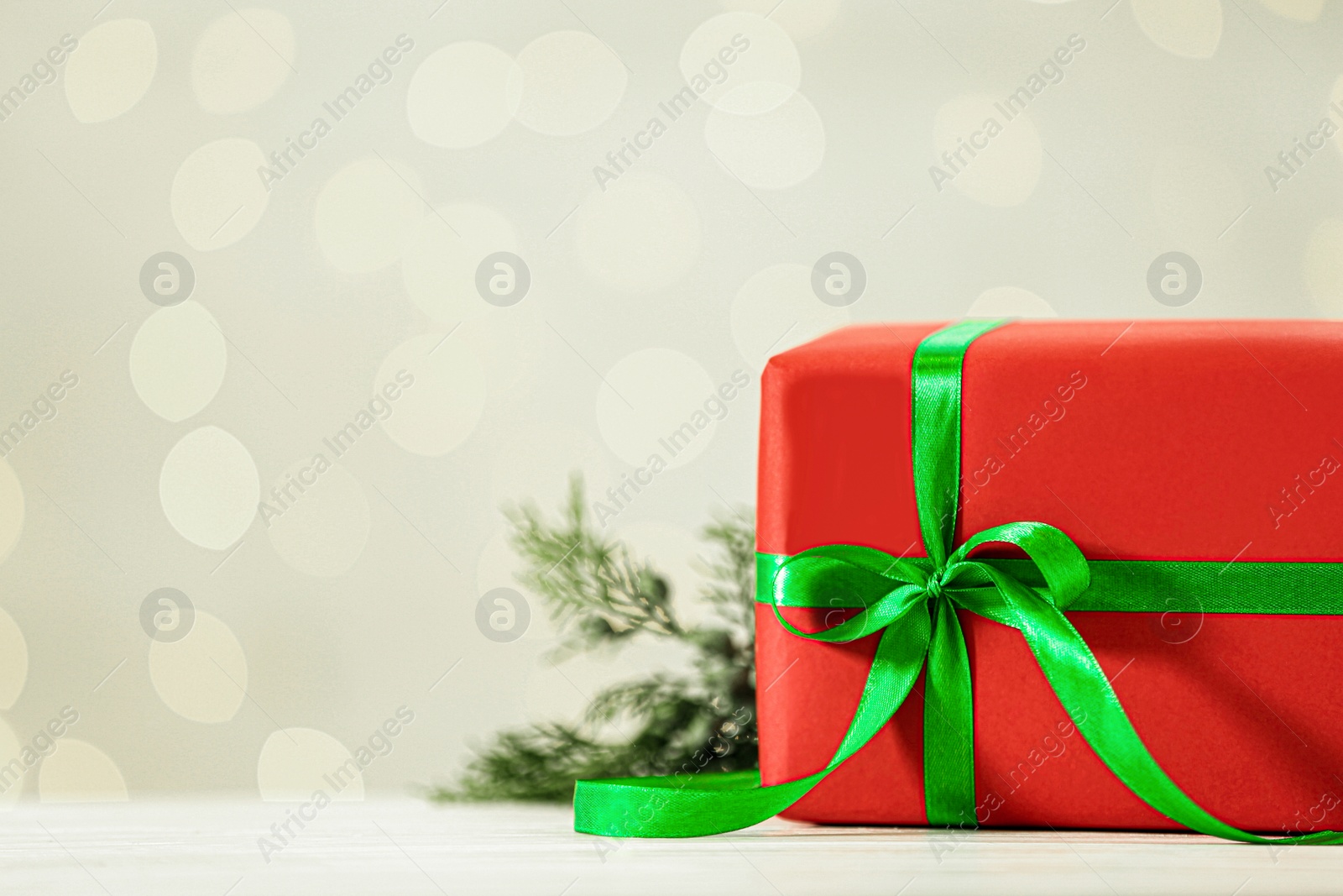 Photo of Christmas gift on wooden table against blurred lights. Space for text