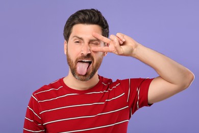 Photo of Man showing his tongue and V-sign on violet background
