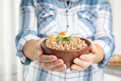 Photo of Woman holding bowl with tasty buckwheat porridge and meat, closeup