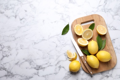 Photo of Many fresh ripe lemons with green leaves and knife on white marble table, flat lay. Space for text