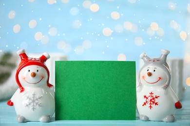 Photo of Decorative snowmen near blank green card on light blue table, space for text