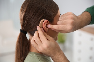 Photo of Young man putting hearing aid in woman's ear indoors