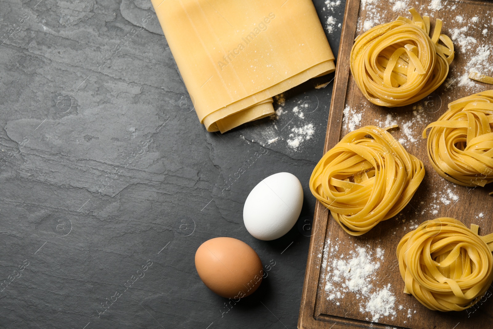 Photo of Raw tagliatelle pasta and products on black table, flat lay