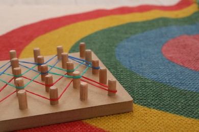 Photo of Wooden geoboard with rubber bands on carpet, closeup. Space for text. Educational toy for motor skills development