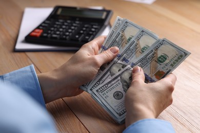 Money exchange. Woman counting dollar banknotes at wooden table, closeup